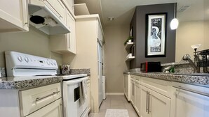 Una cocina con gabinetes blancos, estufa blanca, refrigerador y microondas.