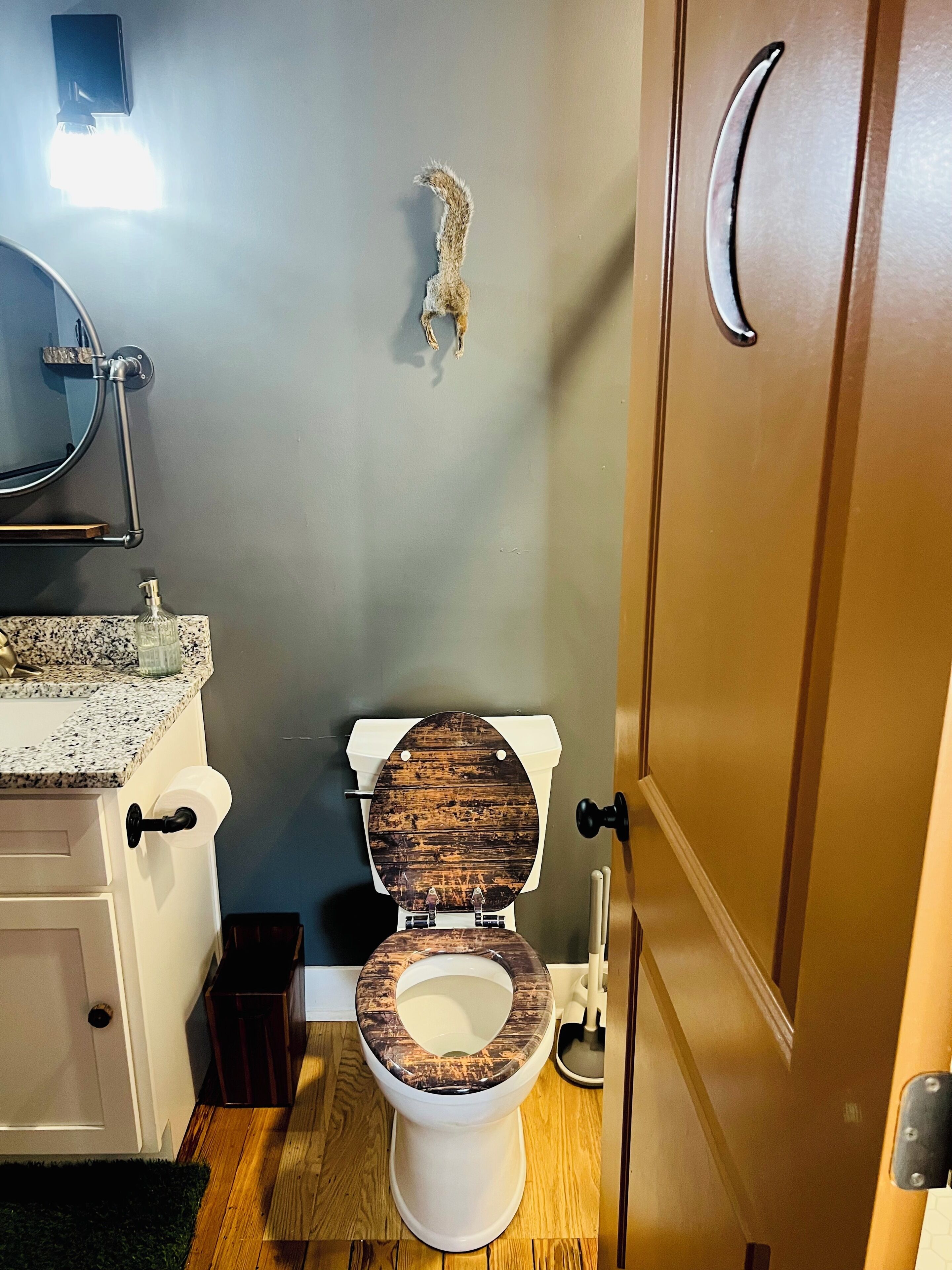 A bathroom with a wooden toilet seat, a sink with a granite countertop, a wall-mounted light, and a door with a silver handle.