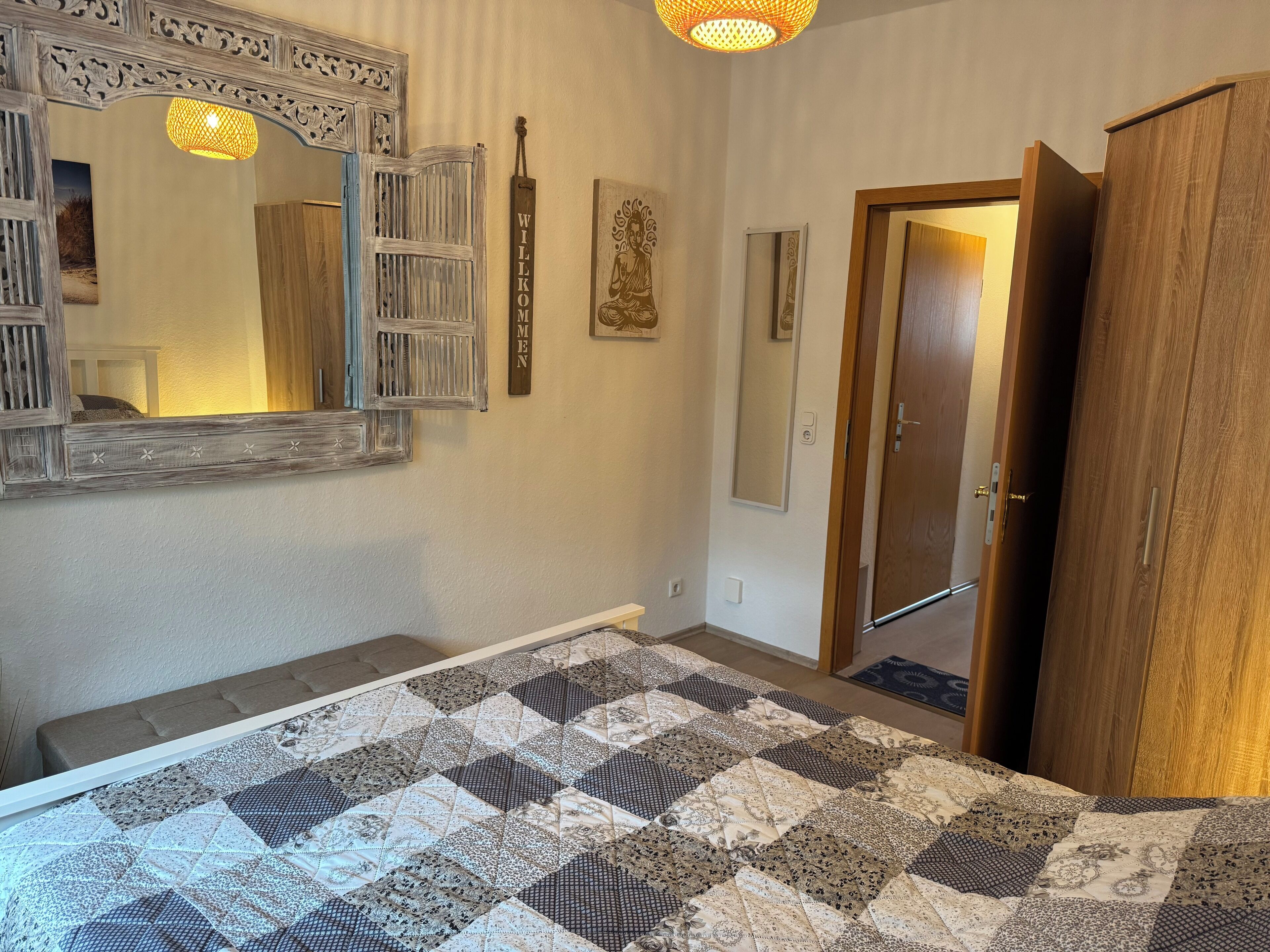 A bedroom with a large bed, a wooden wardrobe, a mirror with a decorative frame, and a quilt on the floor.