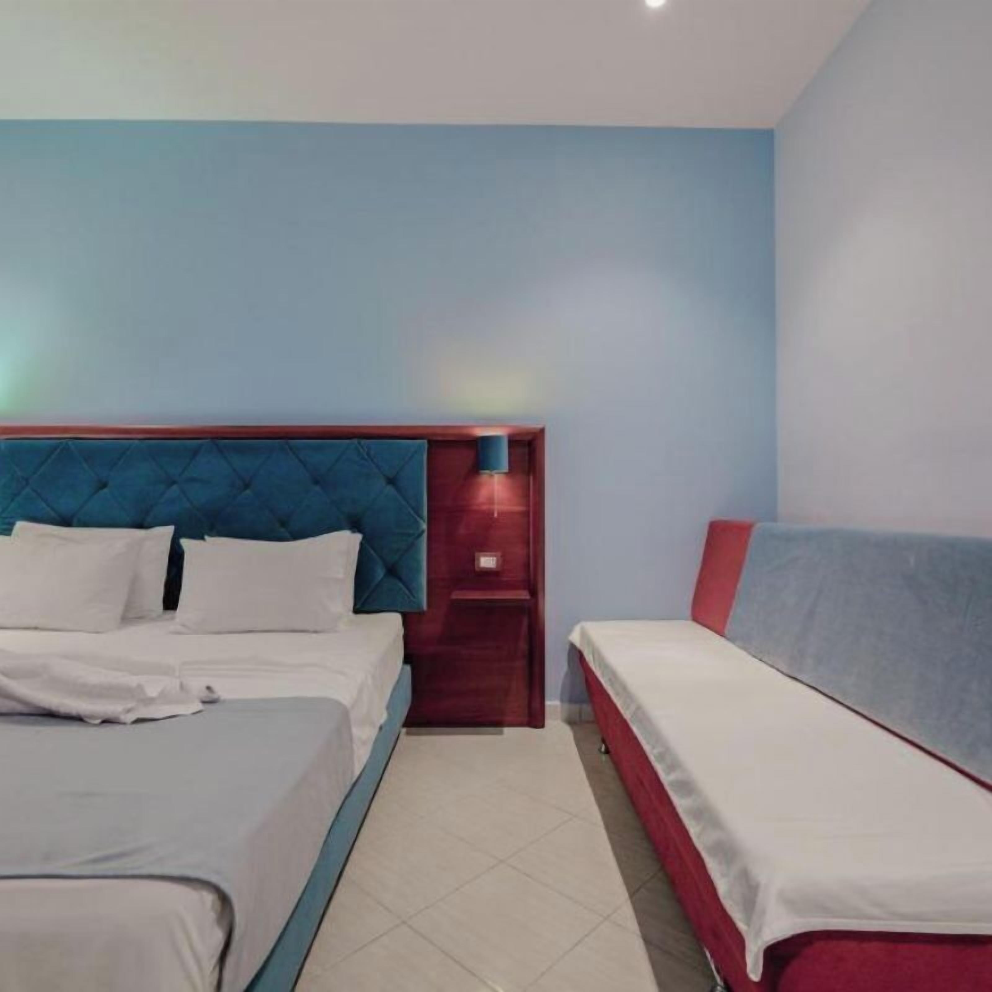 A hotel room with a large bed, a smaller bed, and a nightstand with a lamp.