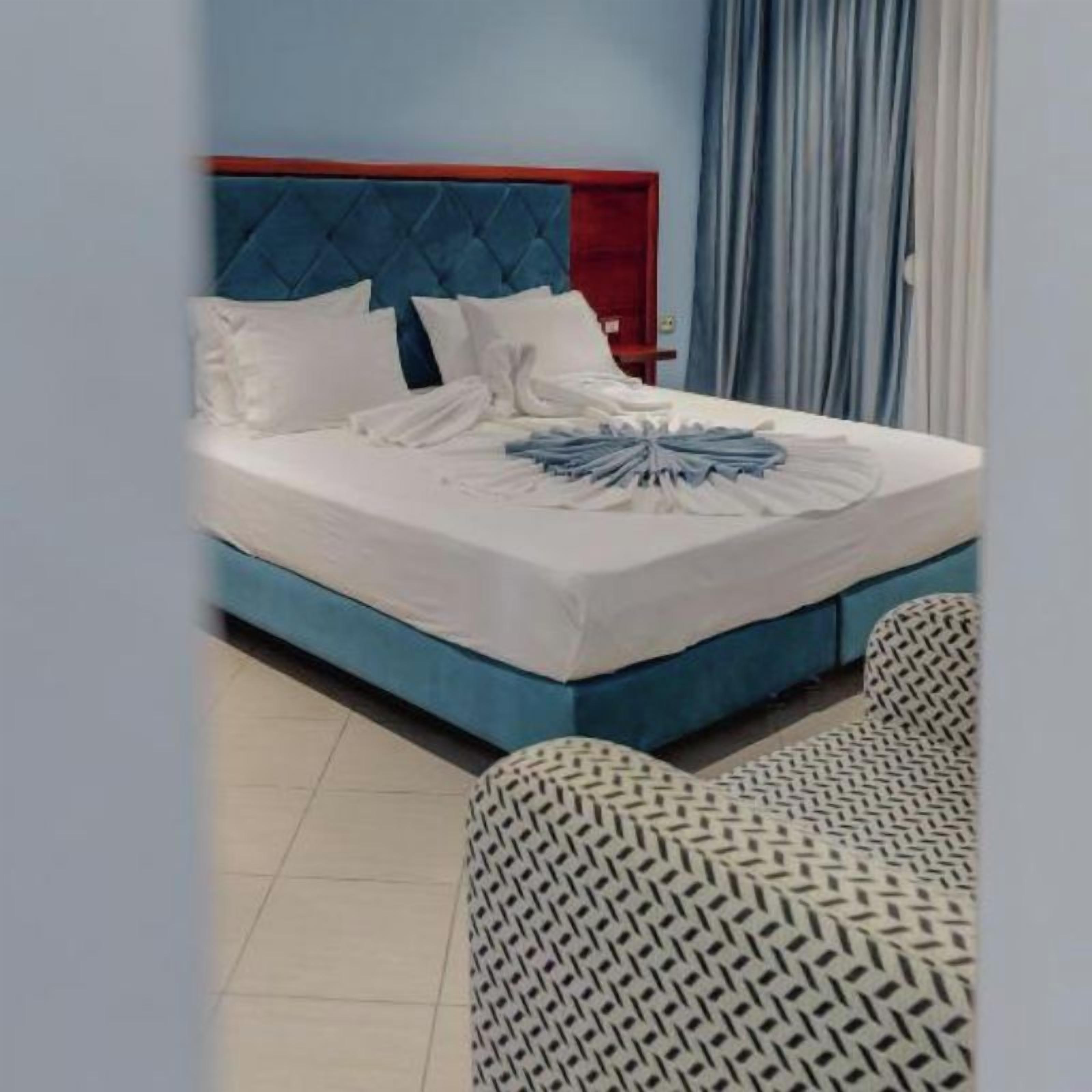 Une chambre d’hôtel avec un lit bleu, des oreillers blancs et une couverture soigneusement disposée.