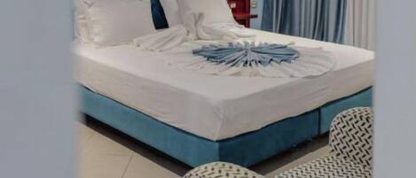 Une chambre d’hôtel avec un lit bleu, des oreillers blancs et une couverture soigneusement disposée.