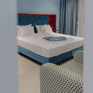 Ein Hotelzimmer mit einem blauen Bett, weißen Kissen und einer ordentlich bezogenen Bettdecke.