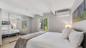 A modern bedroom with a large bed, a glass partition, and a window with a view of greenery.