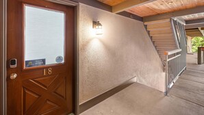 A wooden door with a number plate, a textured wall, and a staircase with metal railings.
