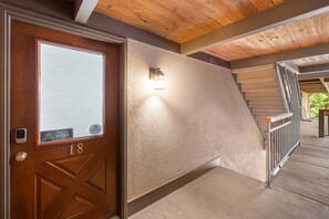 A wooden door with a number plate, a textured wall, and a staircase with metal railings.