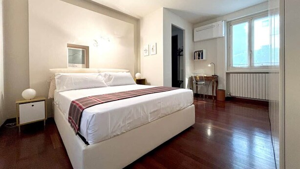 A bedroom with a bed, bedside tables, a mirror, a radiator, and a window. - COMO mi CASA • Lakefront • Ideal Base for Visiting the Lake (Malgrate)