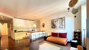 A modern living room with a sofa, a round ottoman, a dining area with a bar, and a kitchen in the background. - COMO mi CASA • Lakefront • Ideal Base for Visiting the Lake (Malgrate)