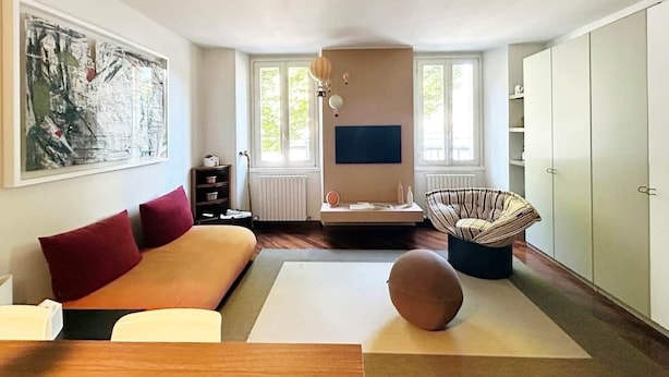 Moderni olohuone, jossa on sohva, pyöreä pöytä, tuoli, televisio ja vaatekaappi.