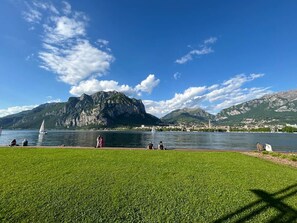 Ein See mit einem Segelboot, Menschen am Ufer und Bergen im Hintergrund.