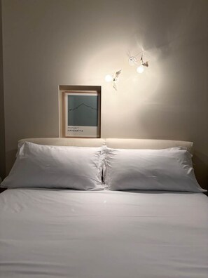 A bed with white linens, a framed chart on the wall, and two wall-mounted light fixtures.