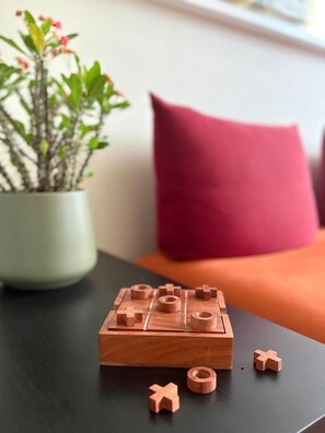 Ein Holz-Brettspiel auf einem Tisch, im Hintergrund ein Blumentopf und ein rotes Kissen.