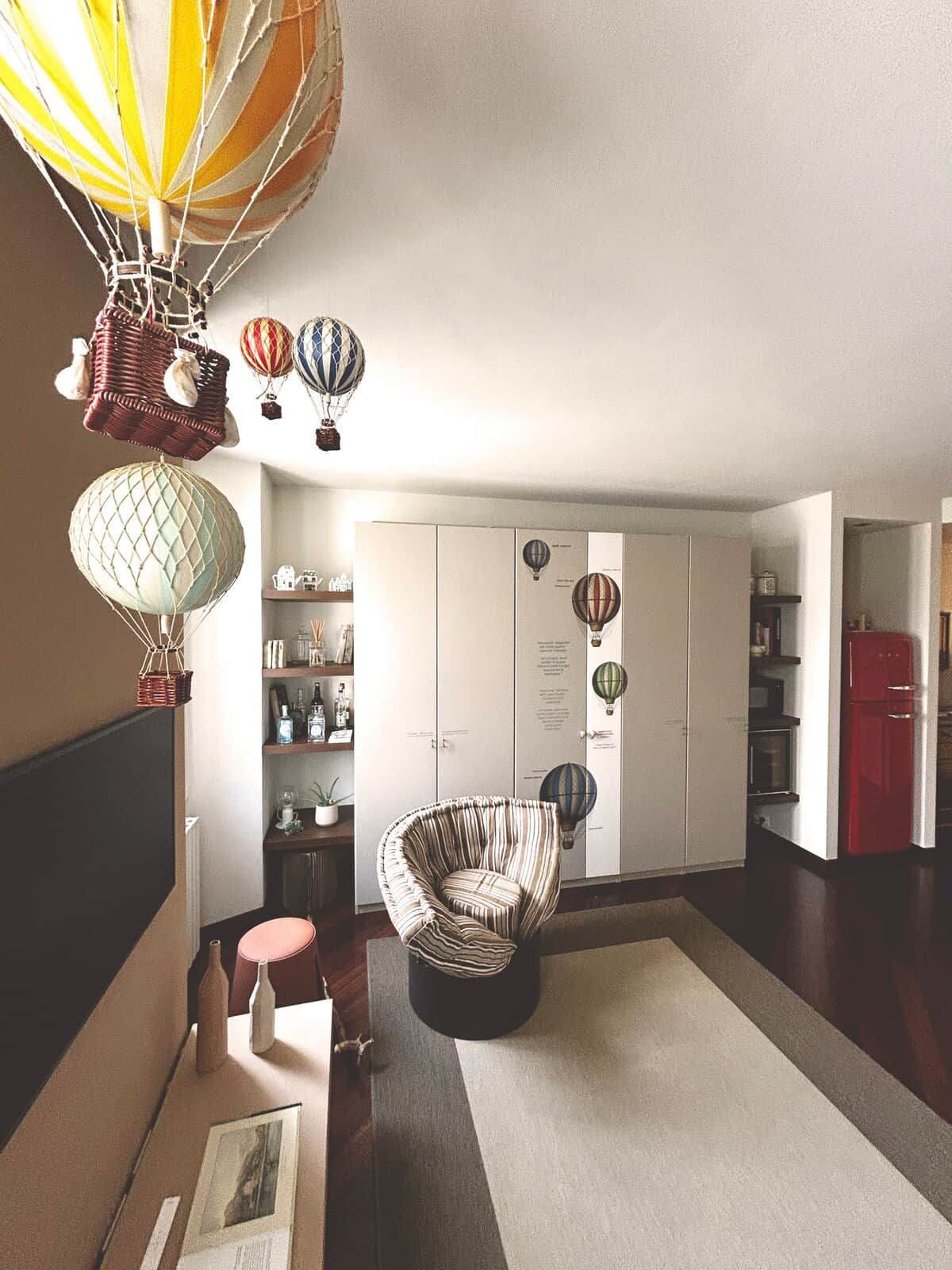 Ein Zimmer mit einem Korbstuhl, einem roten Schrank und einem weißen Kleiderschrank mit Heißluftballon-Verzierungen.