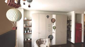 Ein Zimmer mit einem Korbstuhl, einem roten Schrank und einem weißen Kleiderschrank mit Heißluftballon-Verzierungen.