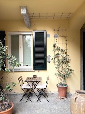 A patio with a table and chairs, a window with shutters, a potted plant, and a wall-mounted plant holder. - COMO mi CASA • Lakefront • Ideal Base for Visiting the Lake (Malgrate)