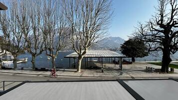 Ein Park am Wasser mit überdachter Sitzgruppe, Bäumen und einem Radfahrer.