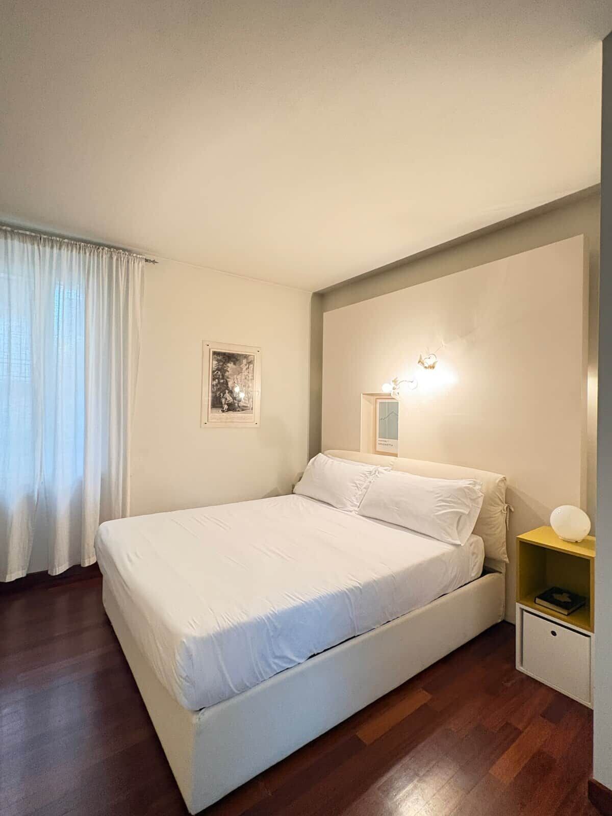 Ein Schlafzimmer mit Bett, Nachttisch, Wandlampe und einem gerahmten Bild.