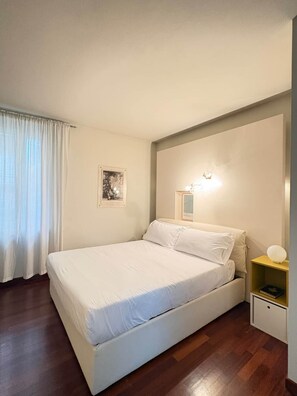 Une chambre à coucher avec un lit, une table de chevet, une lampe fixée au mur et un tableau encadré.