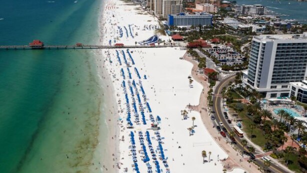 A coastal cityscape with a wide beach, a pier, and several high-rise buildings.