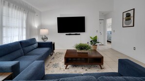 A modern living room with a blue sofa, a wooden coffee table, and a flat-screen TV mounted on the wall.