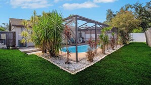 A backyard with a pool, a covered patio, and a well-maintained lawn.