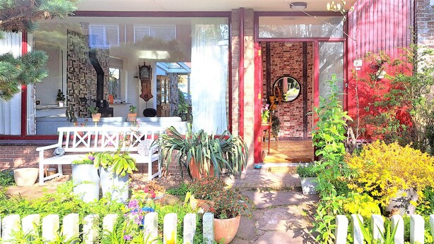Une maison avec un porche à l’avant, des plantes en pot et un mur en briques.