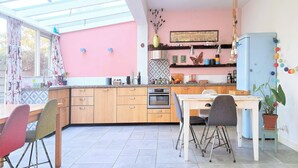 Une cuisine avec des meubles de rangement en bois, une table à manger avec des chaises, un réfrigérateur bleu et une plante suspendue.