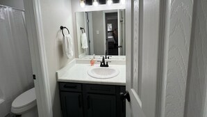 Un bagno con un lavandino bianco, mobili neri, uno specchio illuminato e un asciugamano appeso al muro.