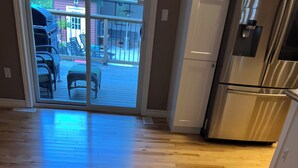 A kitchen with wooden flooring, a stainless steel refrigerator, and a sliding glass door leading to an outdoor area with chairs and a table. - Pool and Hot Tub ,4 Bedroom  .3 Full Bath (Burk’s Falls)