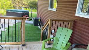 A wooden deck with a green chair and a table, a hot tub, and a small window. - Pool and Hot Tub ,4 Bedroom  .3 Full Bath (Burk’s Falls)