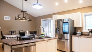 A modern kitchen with stainless steel appliances, a dishwasher, and a dining area with a checkered tablecloth. - Pool and Hot Tub ,4 Bedroom  .3 Full Bath (Burk’s Falls)
