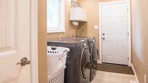 A laundry room with two front-loading washing machines, a white laundry basket, a white cabinet above the machines, and a white door. - Pool and Hot Tub ,4 Bedroom  .3 Full Bath (Burk’s Falls)