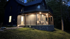 A two-story house with a balcony, stone foundation, and a dark roof.