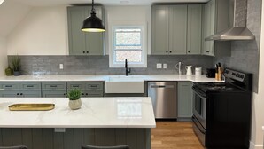 A modern kitchen with a central island, stainless steel appliances, and light green cabinetry.