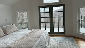 A bedroom with a bed, a ceiling fan, a large window, and a door leading outside.