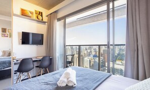 A hotel room with a bed, a desk, two chairs, a TV, and a large window with a city view. - Charming, Well-located apt in Paraiso Onp2021 (São Paulo)