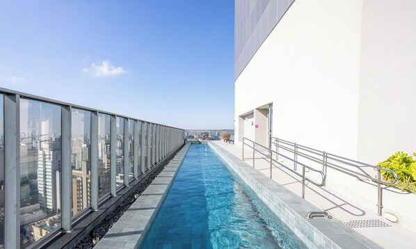 A long, narrow pool with clear blue water, surrounded by a glass railing on one side and a white building on the other. - Charming, Well-located apt in Paraiso Onp2021 (São Paulo)