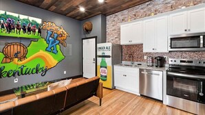A modern kitchen with white cabinets, stainless steel appliances, and a brick accent wall. - Kentucky State of Mind - Interactive Puzzle Stay (Frankfort)
