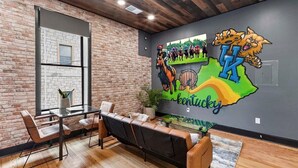 A modern interior with a brick wall, a large window, a mural of a horse race, and a seating area with leather chairs and a glass table. - Kentucky State of Mind - Interactive Puzzle Stay (Frankfort)