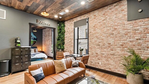 A modern living room with a leather sofa, a coffee table, and a brick wall. There is a sign that reads "Bourbon" on the wall. - Kentucky State of Mind - Interactive Puzzle Stay (Frankfort)