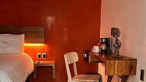 Une chambre comprenant un lit, un bureau en bois, une chaise, une petite table avec une machine à café et un tapis à motifs.