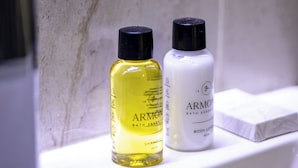 Deux bouteilles de produits de bain sont posées sur une étagère blanche dans une salle de bain dont les carreaux ont une texture particulière.