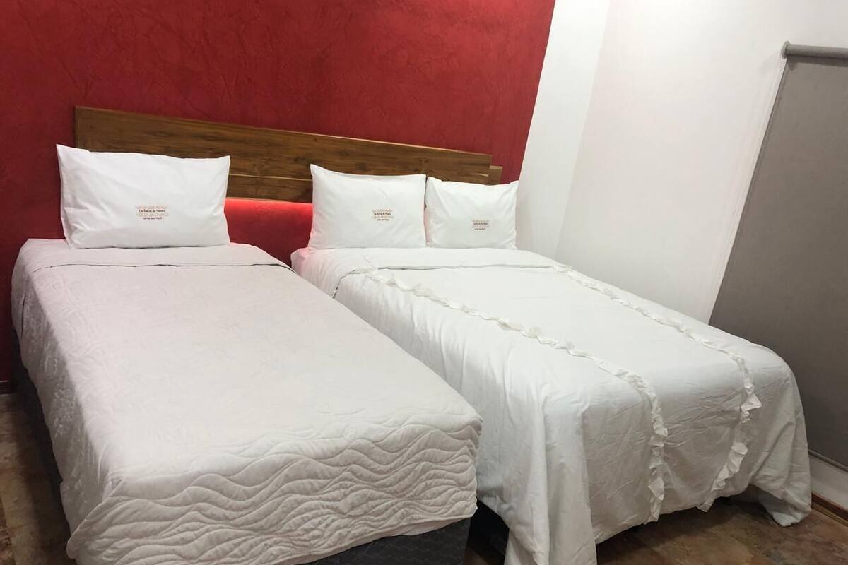 Una habitación con dos camas, cada una con ropa y almohadas blancas, cabeceros de madera y una pared roja.