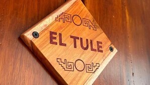 Une plaque en bois portant l’inscription « EL TULE » et ornée de motifs décoratifs.