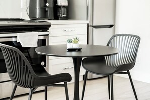 Una cocina moderna con una mesa redonda, dos sillas negras, una cafetera y un refrigerador.