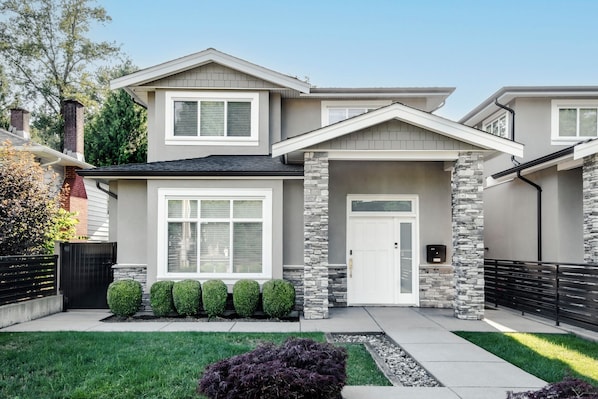 A modern two-story house with a stone facade, a garage, and a well-maintained front yard.