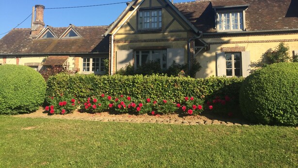 A two-story house with a gabled roof, a chimney, and a garden with red flowers. - Charming family farmhouse in the countryside (Rueil-la-Gadelière)