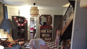 A cozy living room with a sofa, armchair, and a patterned rug. A bookshelf and a staircase are visible in the background. - Charming family farmhouse in the countryside (Rueil-la-Gadelière)