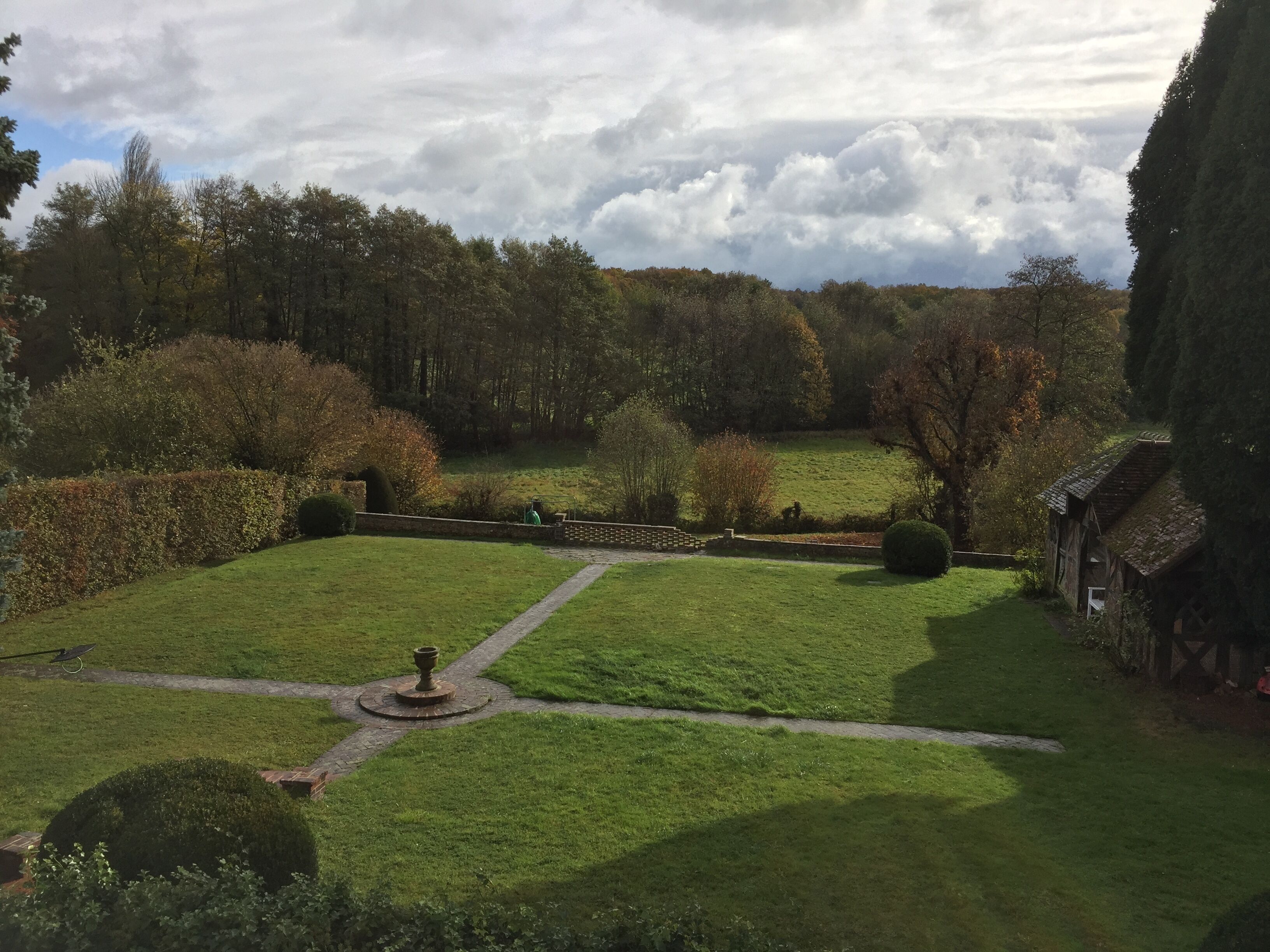 Un jardin bien entretenu, avec un chemin central, bordé de haies et d’arbres taillés avec soin.