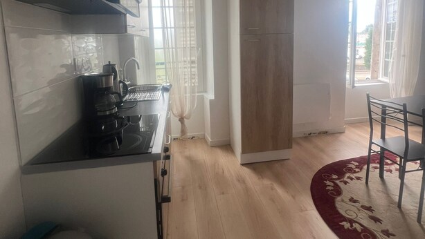Une cuisine moderne équipée d’une cuisinière, d’un évier et de placards, un coin repas avec une table et des chaises, et une grande fenêtre avec des rideaux.